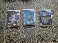 Photo of three Wii game cases laying on a patterned carpet showing titles: The Bigs, The Golden Compass, The Black Eyed Peas Experience.