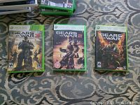 Photo showing three Xbox 360 game cases for Gears of War series lined up side by side on patterned carpet.