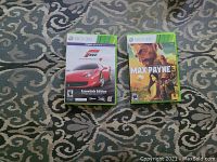 Photo showing two Xbox 360 game cases on patterned carpet: Forza Motorsport 4 Essentials Edition and Max Payne 3.