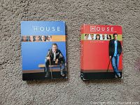 Photo showing two DVD box sets of the TV series House: Season 1 in blue and Season 3 in red, both with images of the lead character Dr. House.