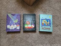 Three DVD box sets displayed on carpet: South Park Season 4 and Season 1, and The Simpsons Season 3.