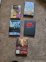 Five DVDs arranged on carpet: The History of Rome, Monty Python Live, Lost Season One, Sin City, and The Crusades.