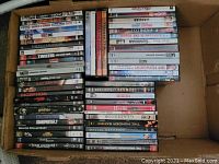 Box of assorted DVDs with visible titles including Inception, Million Dollar Baby, Harry Potter, Saw II, Transformers 2, and more.