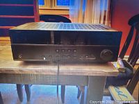 Black Yamaha AV receiver atop wooden table, front view showing controls, headphone jack, and large volume knob, with ventilation slots on the top.