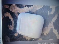 Photo of closed Apple AirPods charging case with Apple logo visible resting on patterned fabric surface.