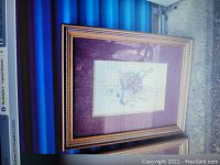 Photo showing one framed floral botanical artwork with purple textured matting and gold-tone wooden frame.