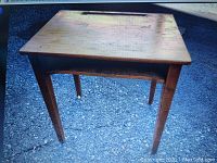 Photo of a small handmade wooden desk showing the top surface and four legs on a concrete surface.