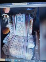 Wingback armchair with floral and stripe patterned fabric upholstery in a dimly lit room next to wooden chair.