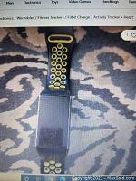 Photo shows a Fitbit Charge 3 device with a black and yellow perforated sport band on a patterned fabric background.