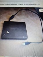 Photo of the LG external drive connected to a USB cable, showing the top surface and connectivity cable.