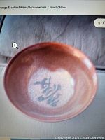 Image shows a reddish-brown ceramic bowl with Chinese calligraphy at the center interior base.