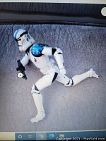 White Stormtrooper figure with blue details, posed running and holding a blaster gun on a grey fabric background.