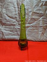 Front view of the tall greenish glass vase with three small legs, hobnail texture, and swung top