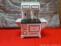 Front view of white ceramic cookie jar shaped like vintage wood stove with black stovetop and red detailing on doors and drawers.