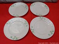 Four white porcelain dessert plates arranged on red fabric, showing the shamrock pattern and textured rims.