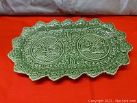 Green cabbage ware ceramic serving platter with textured cabbage edges and two rabbit medallions taken on red fabric background.