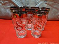 Set of nine tall cocktail tumblers with platinum rims and letter S monogram arranged on a red surface.