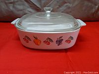 Side view of white ceramic casserole dish with Fruit Basket pattern and clear glass lid on top.