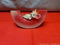 Front view of vintage plastic watermelon still bank with crying mouse detail on top, showing holes marking watermelon seeds.