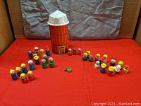 Photo showing orange wooden silo toy with white top surrounded by 33 assorted wooden Little People figures in red, blue, green, and yellow colors with hand painted facial details.