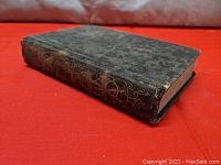 Book laying flat showing front cover with worn black cover and gold decorative spine details