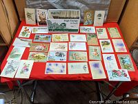 Wide view of various vintage and antique postcards displayed on a red surface, showing floral and holiday designs.