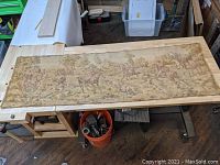 Full view of the large rectangular fox hunting tapestry laid flat on a wooden table, showing the overall scene of horse riders and dogs.