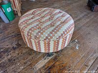 Side angled view showing tufted top and fabric pattern of brown and orange polka dot stripes on beige background, placed on worn wooden floor.
