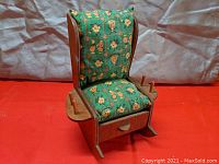 Full view of the pin cushion in the form of a wooden rocking chair with a green floral patterned cushion, showing thread holder pegs on either side and the drawer below.