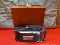 Polaroid 900 Land Camera in front of brown leather carrying case on red background
