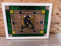 Photo of first stained glass panel with green border and yellow, dark blue Celtic knot center design.