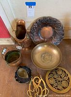Photo showing the assorted copper items including pitcher, ornate tray, bowl, pot, ladle with stone base, and trivets.