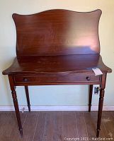 Front view of vintage wooden desk with high curved back and tapered legs.