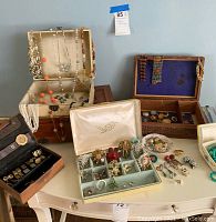 Overview of three open jewelry boxes and trays showing various brooches, necklaces, bracelets, rings and cufflinks arranged on a table.