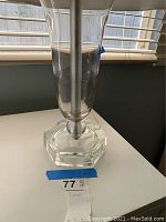 Clear glass hurricane style table lamp with hexagonal base on a white surface by window.