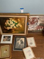 Overview of all wall art pieces arranged on floor leaning against wall including large floral painting, tiger print, and smaller framed pictures.