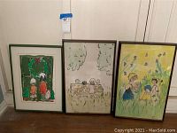 Three framed child paintings in a row leaning against a wall.