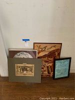 Group view of five assorted wall art items leaning against a wall showing variety in size, matting and framing
