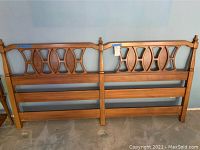 Full view of the wooden headboard showing the geometric cutout design and the two main sections connected centrally with finials.