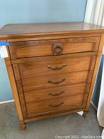 Front angle view of wooden highboy dresser with brass drawer handles and tapered legs.