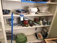 Shelf with white ceramic soup tureen, blue and white bowls, keepsake boxes, and mugs arranged on three shelves.