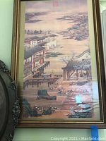 Close-up of a framed vintage Asian artwork showing a traditional waterfront building, bridge, and nature scene with silk fabric texture.