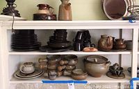 Shelf view with stacked plates, bowls, cups, teapot, and rolling pins among other pottery items.