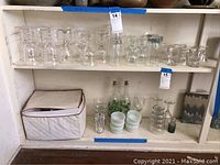 Shelf with multiple clear wine glasses, small frosted bowls, decorative glass bottles and small containers.