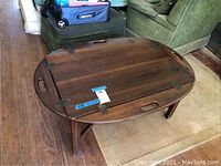 Oval wooden coffee table with sides down and top view showing wood grain and handles.