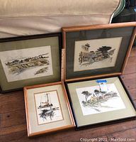 Four framed watercolor and ink artworks arranged on floor showing coastal and town scenes from Mendocino, CA.