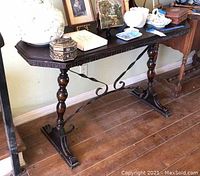 Full side view of vintage wooden sofa or wall table showing rectangular top, worn surface, turned wooden legs, and twisted metal supports between legs.