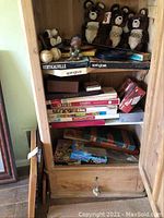Shelf with stacked board games including Scrabble, Clue, Monopoly, and Springbok Verticaville, along with several Misha teddy bears and some smaller items.