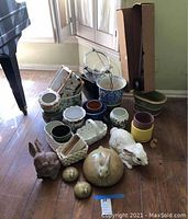 Overview of assorted pottery and ceramic planters, including various pots, decorative rabbits, and garden items arranged on wooden floor.