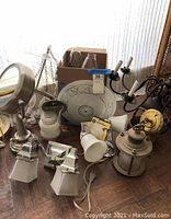 Various lighting fixtures arranged on floor including chandelier, glass shades, metal lantern, and decorative panels